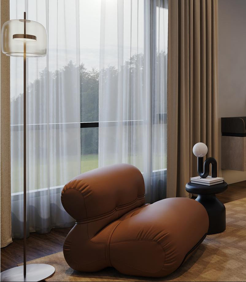 Modern interior with a brown leather chair, floor lamp, and large window with curtains.